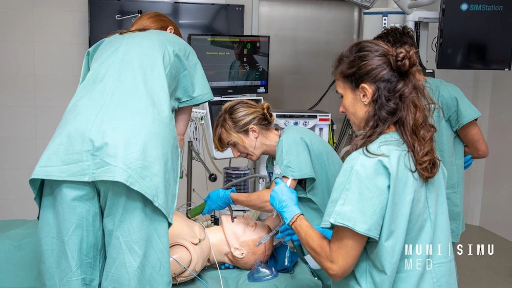 Healthcare team in green scrubs performing intubation on mannequin during emergency simulation, monitor shows saturation signal low.