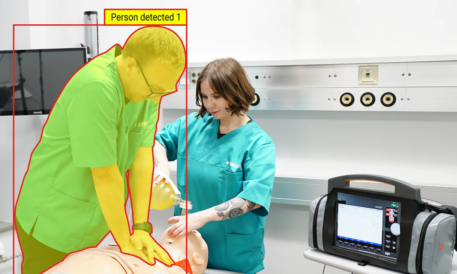 Medical simulation training with healthcare professionals performing airway management on mannequin, supported by AI person detection and vital signs monitoring.